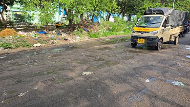 Damaged road with litter, trees, and a yellow truck on a sunny day in an urban area.