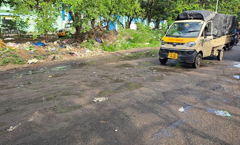 Damaged road with litter, trees, and a yellow truck on a sunny day in an urban area.