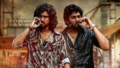 Two men with long hair and beards talking on mobile phones in an industrial setting.