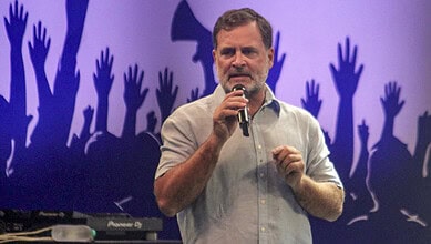 Rahul Gandhi speaking at a rally with raised hands in the background.