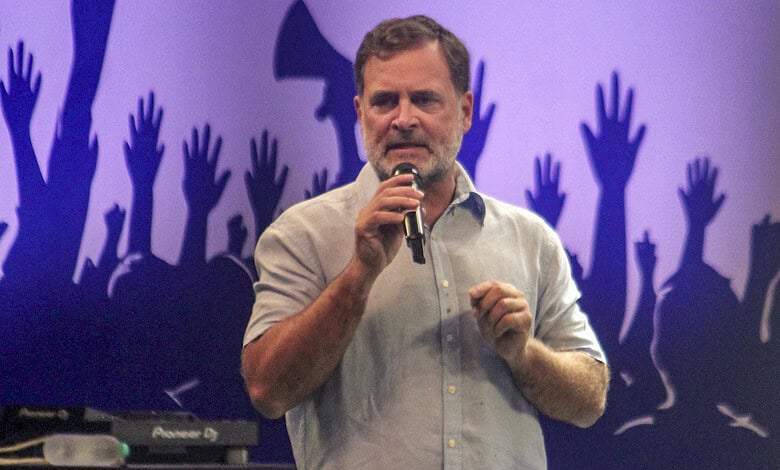Rahul Gandhi speaking at a rally with raised hands in the background.