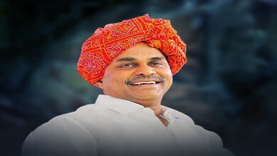 Smiling man wearing a traditional red and orange turban and white attire.