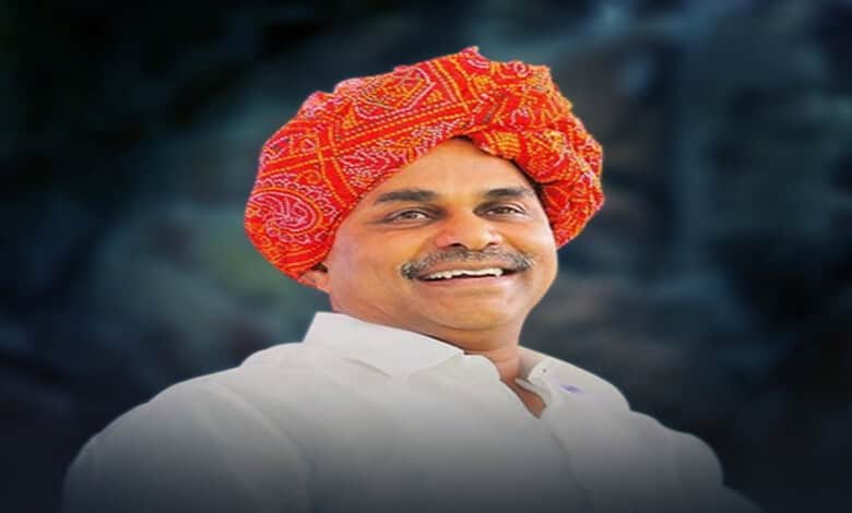 Smiling man wearing a traditional red and orange turban and white attire.