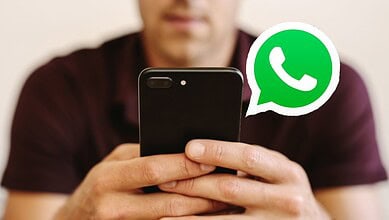 Person holding smartphone with WhatsApp logo visible, engaging in messaging.