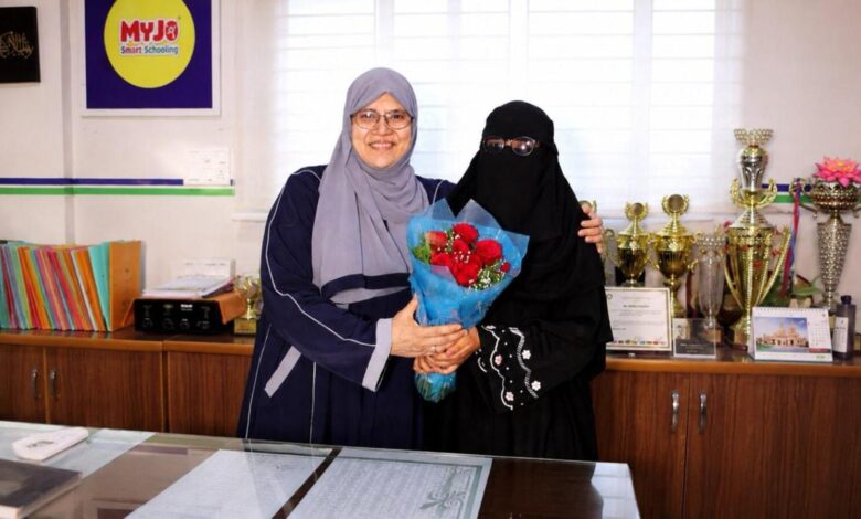 School topper receiving a bouquet from a woman in an office setting with trophies in the background.