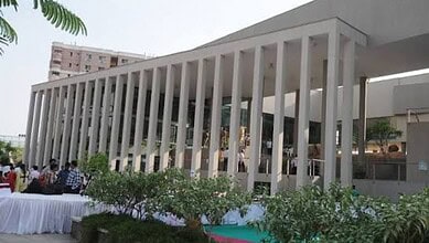 Modern building with vertical white columns and outdoor seating area with people.
