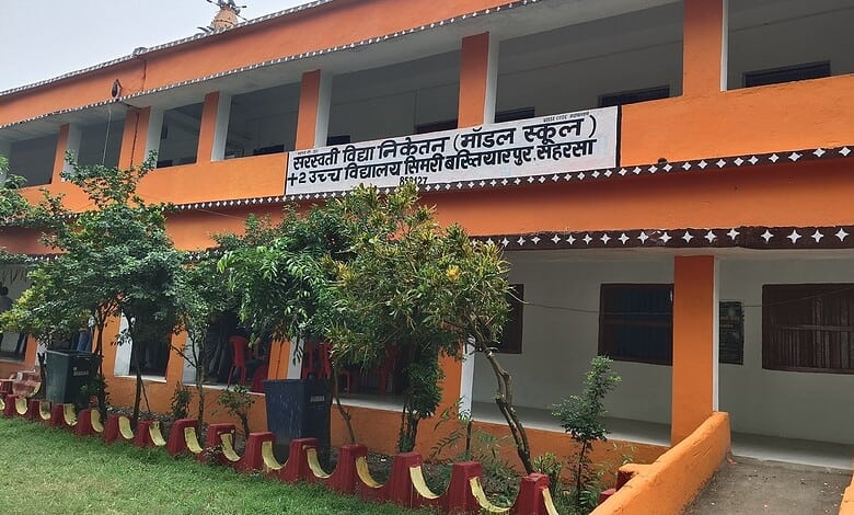 Saffron-coloured school building with a signboard in Hindi and English, surrounded by greenery.