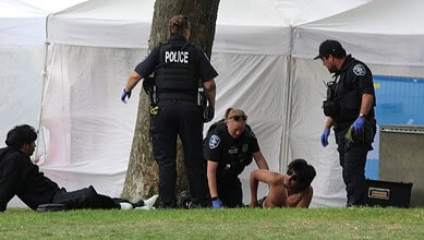 Police officers assist a shirtless man lying on the grass at a crime scene.
