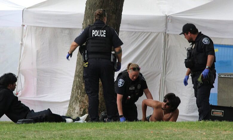Police officers assist a shirtless man lying on the grass at a crime scene.