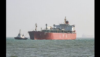 Large cargo ship with tugboat in open sea, under clear sky.