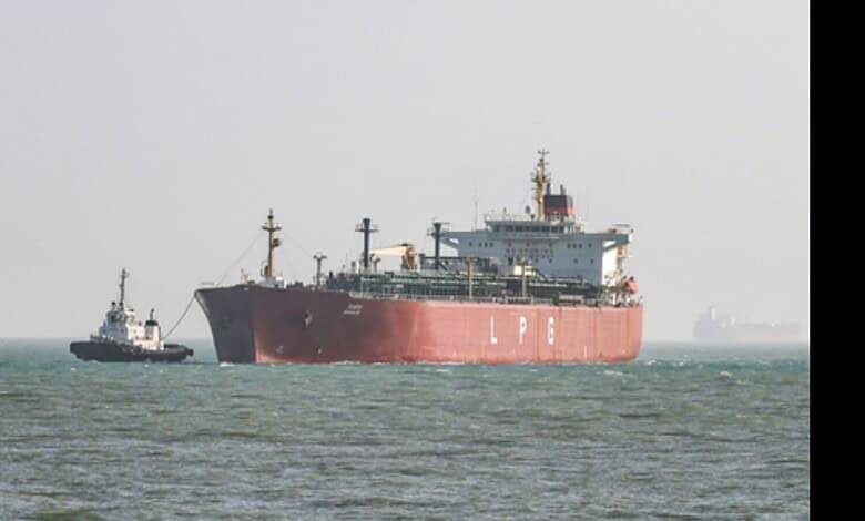 Large cargo ship with tugboat in open sea, under clear sky.