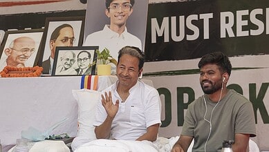 Sonam Wangchuk protesting with a smile at a rally, surrounded by portraits and banners.