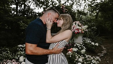 A couple in love touching foreheads in a garden with blooming flowers and greenery.