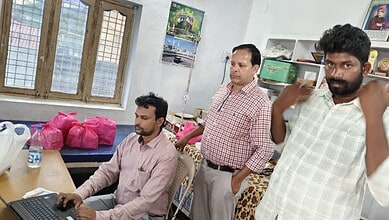 Men in an office, one working on a laptop, others standing, in Khammam.
