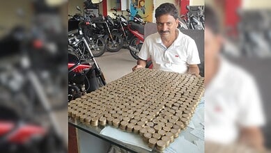 Man sitting at a table with a large collection of Rs 10 coins arranged in a grid.