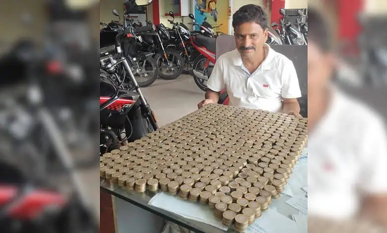 Man sitting at a table with a large collection of Rs 10 coins arranged in a grid.