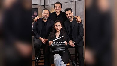Group of five people, three men and two women, posing with a film clapperboard in a studio setting.