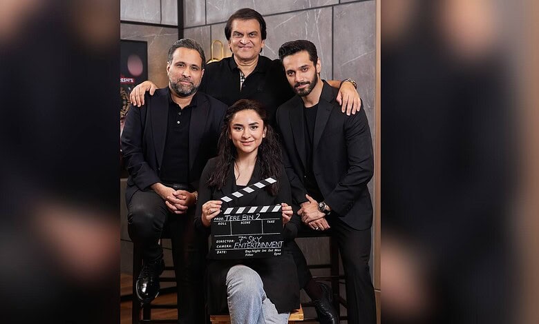Group of five people, three men and two women, posing with a film clapperboard in a studio setting.
