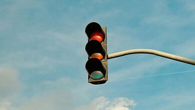 Traffic light showing red signal against a blue sky with clouds.