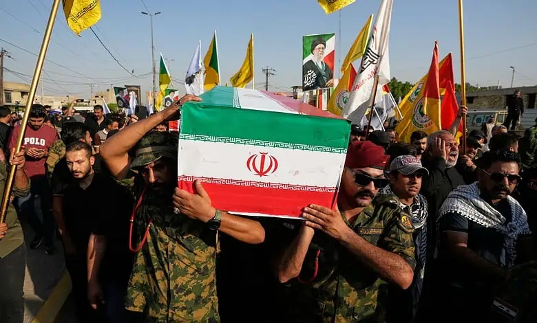 Iranian flag draped over a coffin during a funeral procession with a crowd of mourners and flags in the背景.