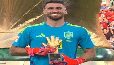 Smiling goalkeeper in blue jersey holding a trophy with gloves, celebrating victory.