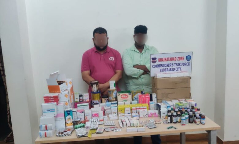 Two men with blurred faces stand behind a table of medicines in Khairatabad.