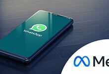 Smartphone displaying WhatsApp logo on a dark wooden surface.