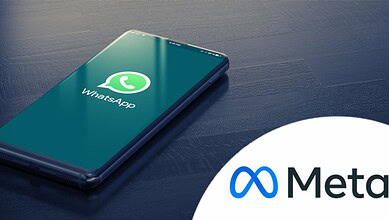 Smartphone displaying WhatsApp logo on a dark wooden surface.
