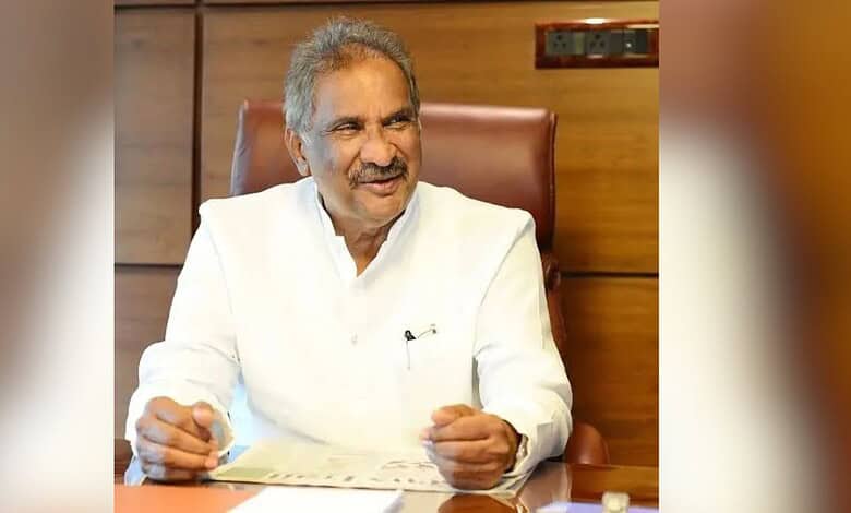 Senior man in white kurta smiling and sitting at a desk in an office setting.
