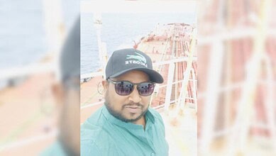 Seafarer wearing sunglasses and cap on a ship deck with ocean background.