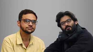 Two men with glasses sitting against a plain grey background.