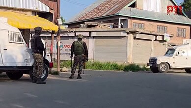 Two armed soldiers in camouflage gear stand on a street in Kashmir during a security operation.