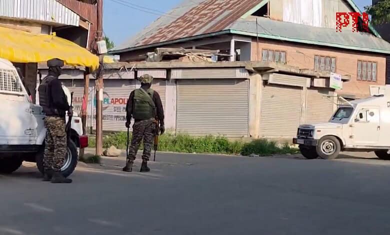 Two armed soldiers in camouflage gear stand on a street in Kashmir during a security operation.