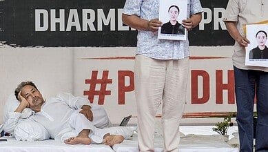 Protest scene with a man lying on the ground and two individuals holding photos of a woman.