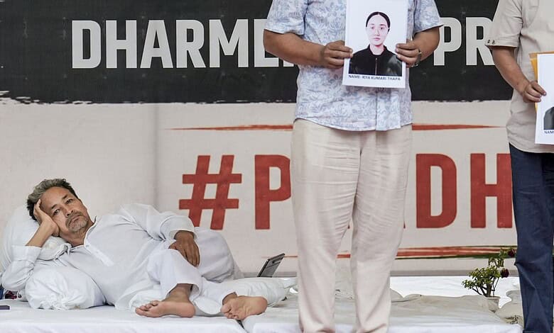 Protest scene with a man lying on the ground and two individuals holding photos of a woman.