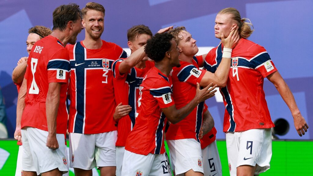 Norwegian football team celebrating during a match, wearing red jerseys with blue and white accents.