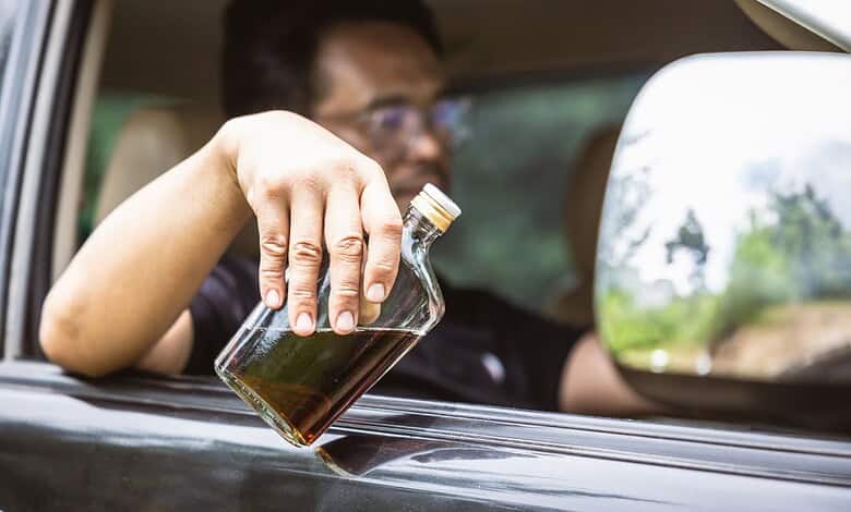 Man holding a bottle of alcohol outside a car window during daytime.