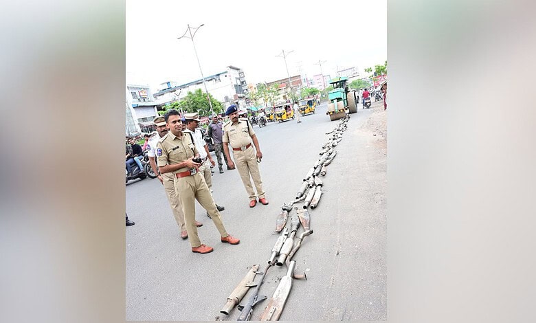 Police officers display a line of confiscated silencers on the road in Adilabad.