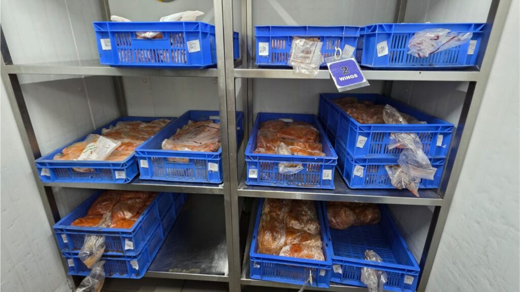 Frozen raw meat stored in blue plastic crates on metal shelves.