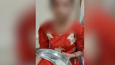 Child with blurred face wearing red dress holding a metal plate in an indoor setting.