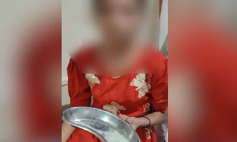 Child with blurred face wearing red dress holding a metal plate in an indoor setting.