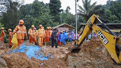 Construction workers and officials at a site with excavator and muddy terrain in a tropical area.