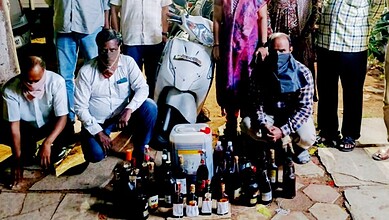 Group of people gathered around a collection of bottles and containers outdoors.