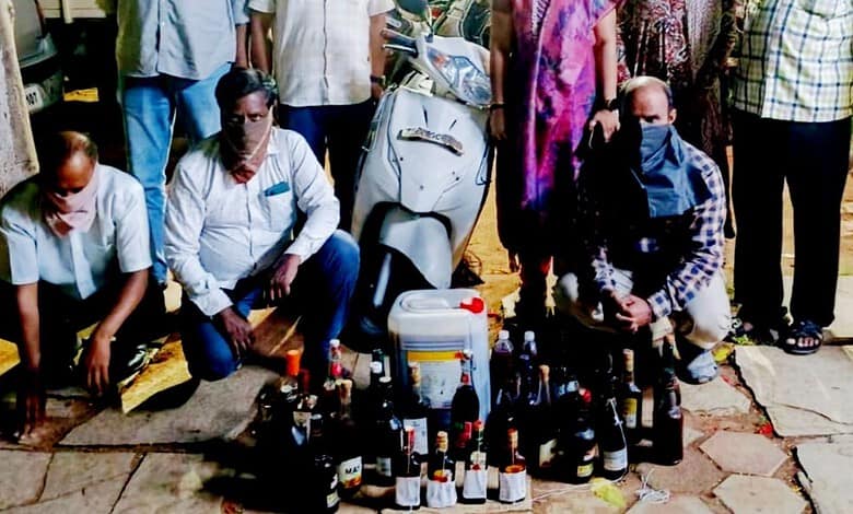 Group of people gathered around a collection of bottles and containers outdoors.