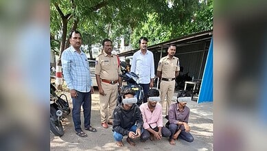Group of men, including police officers, standing outdoors with three seated individuals wearing masks.