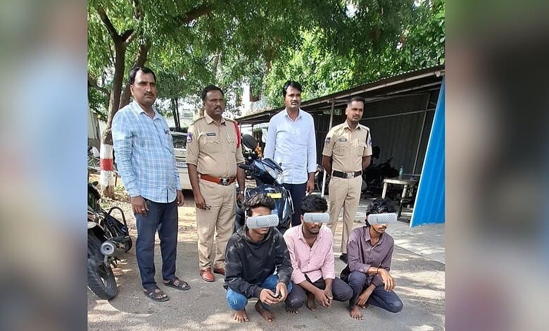 Group of men, including police officers, standing outdoors with three seated individuals wearing masks.