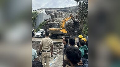 Excavator removing debris from collapsed building caused by garbage mound in Pune.