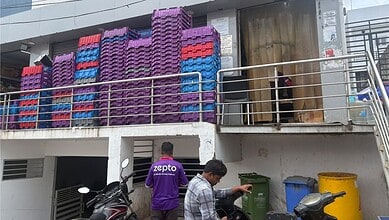 Zepto delivery staff at Narsingi facility during inspection, with stacked crates and waste bins nearby.