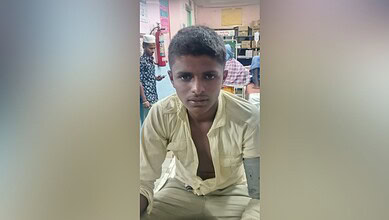 Young boy with serious expression in a classroom setting, wearing a light yellow shirt.