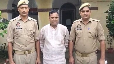 Man in white kurta detained by two police officers outside a building in Uttar Pradesh.